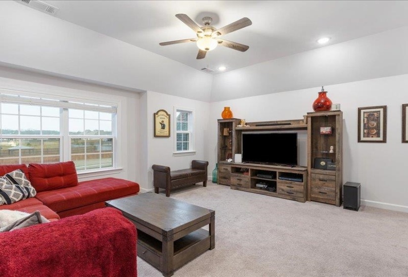 Upstairs bonus room perfect for media, playroom, or flex space. Plush neutral light-colored carpet, a ceiling fan, recessed lighting, and lofted ceiling