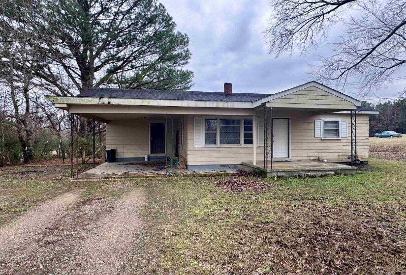 Bungalow-style home with dirt driveway, a carport, a chimney, a front yard, and a patio area