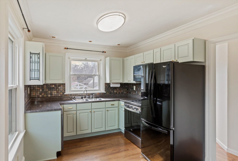 Kitchen featuring dark countertops, freestanding refrigerator, stainless steel range with gas stovetop, ornamental molding, and green cabinets