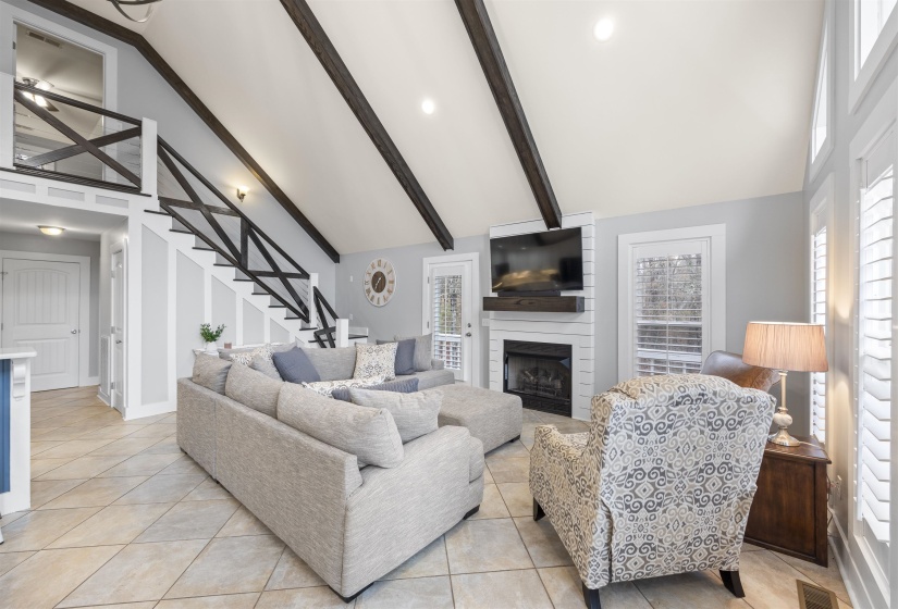 Living area with a large fireplace, high vaulted ceiling, light tile patterned floors, stairs, and beam ceiling