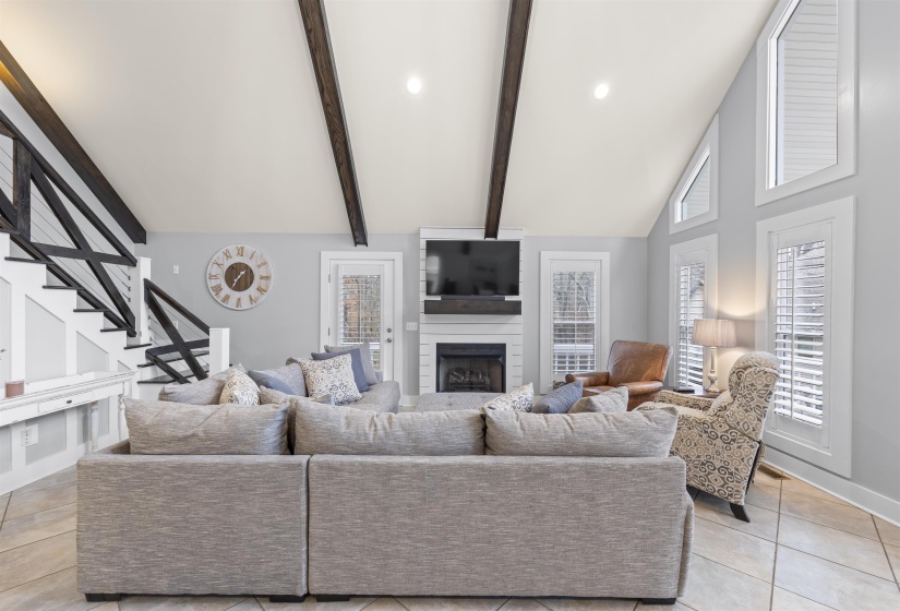 Living area with a large fireplace, light tile patterned floors, beamed ceiling, stairs, and high vaulted ceiling