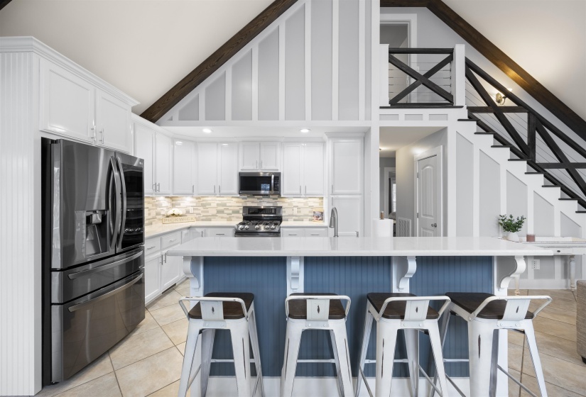 Kitchen with white cabinetry, stainless steel appliances, a kitchen bar, light tile patterned flooring, and high vaulted ceiling