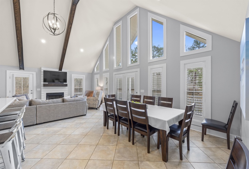 Dining space with a large fireplace, high vaulted ceiling, plenty of natural light, light tile patterned floors, and beamed ceiling