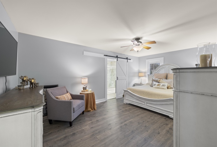 Bedroom with a barn door, ceiling fan, and dark wood-type flooring