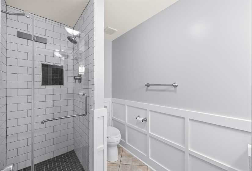 Full bath featuring a wainscoted wall, a decorative wall, a shower stall, and light tile patterned floors