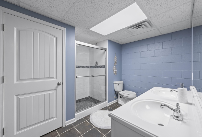 Bathroom with a shower stall, dark tile patterned flooring, double vanity, a drop ceiling, and concrete block wall