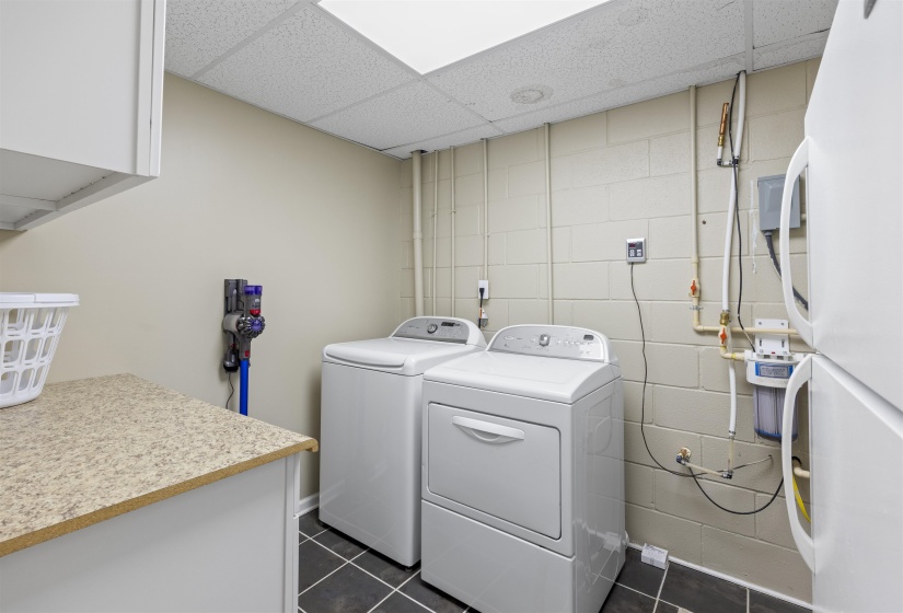 Laundry area with a drop ceiling, dark tile patterned flooring, washing machine and dryer, and concrete block wall