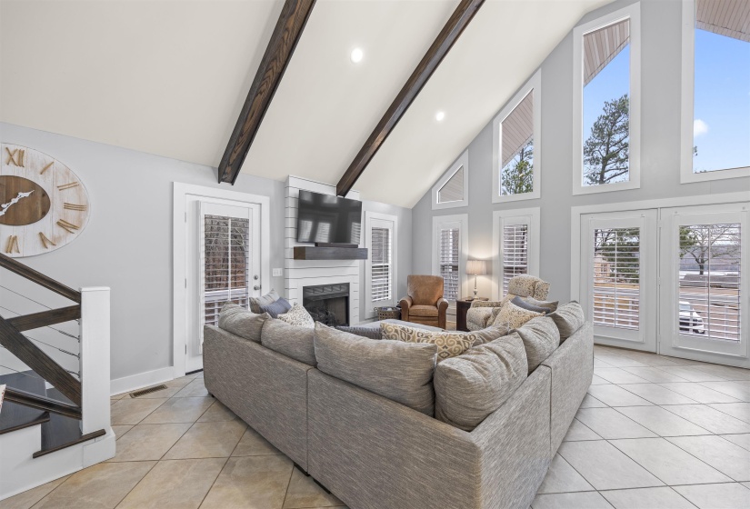 Living room with stairway, light tile patterned floors, high vaulted ceiling, a large fireplace, and beam ceiling