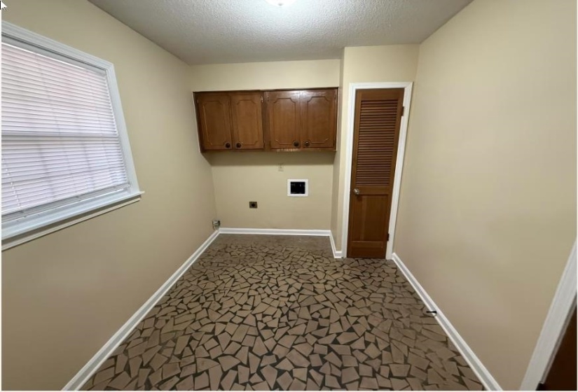 Washroom with a textured ceiling, cabinet space, hookup for an electric dryer, and dark colored carpet