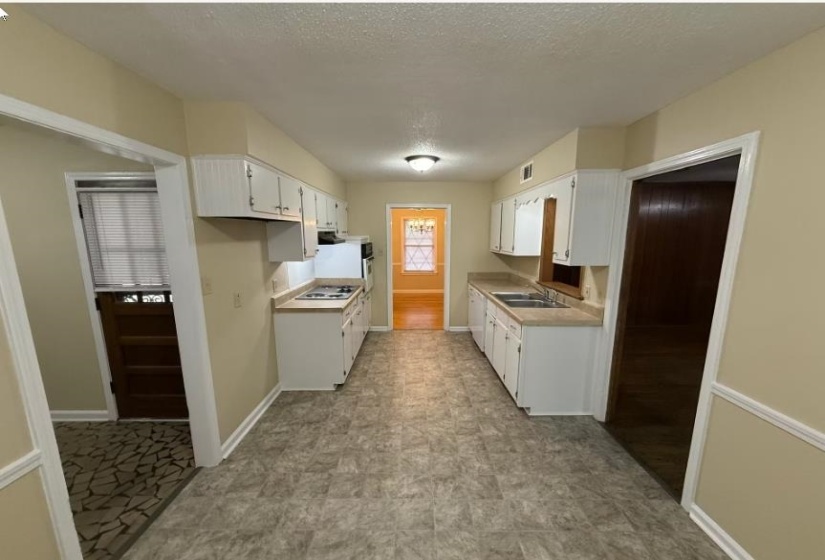 Kitchen with light countertops, a textured ceiling, white cabinetry, and gas cooktop