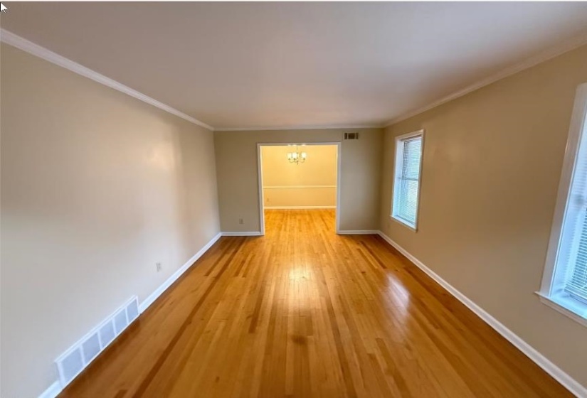 Empty room featuring a chandelier, ornamental molding, and light wood-style flooring