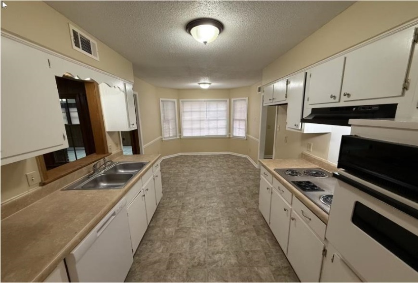 Kitchen with white appliances, a textured ceiling, white cabinetry, light countertops, and under cabinet range hood