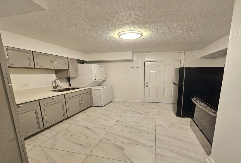 Kitchen with gray cabinets, stacked washer / drying machine, light marble finish flooring, stainless steel appliances, and a textured ceiling