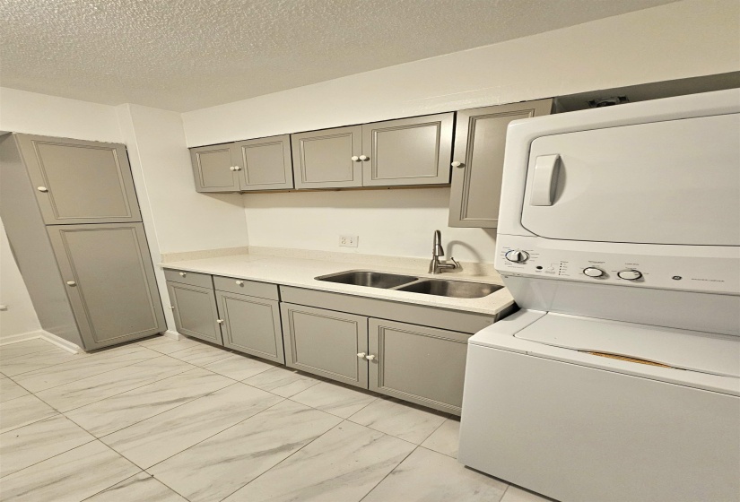 Laundry area with cabinet space, light marble finish flooring, stacked washer and clothes dryer, and a textured ceiling