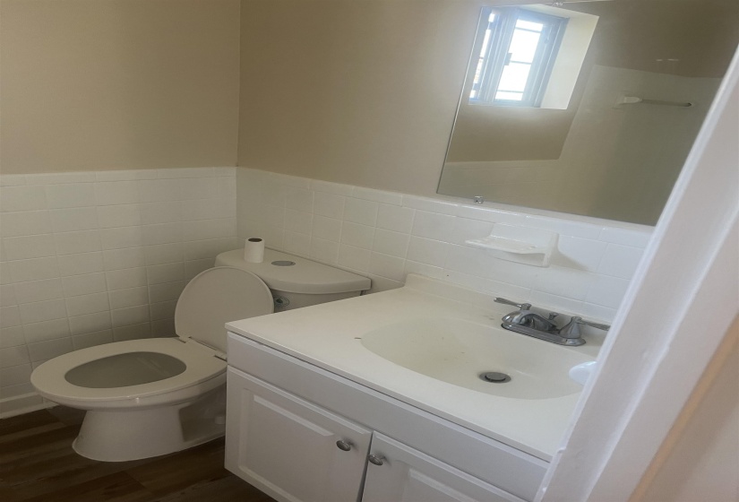 Half bathroom featuring vanity, dark wood-style floors, wainscoting, and tile walls