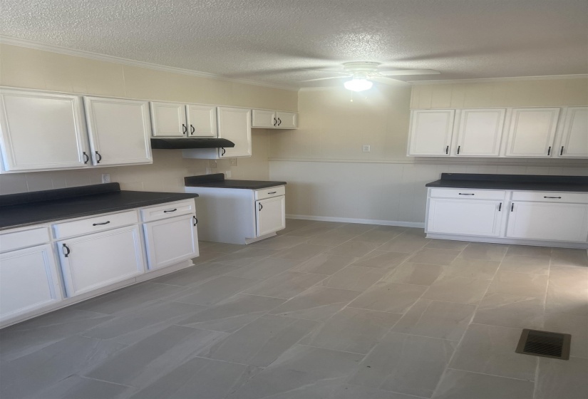 Kitchen featuring dark countertops, white cabinetry, a textured ceiling, crown molding, and a ceiling fan