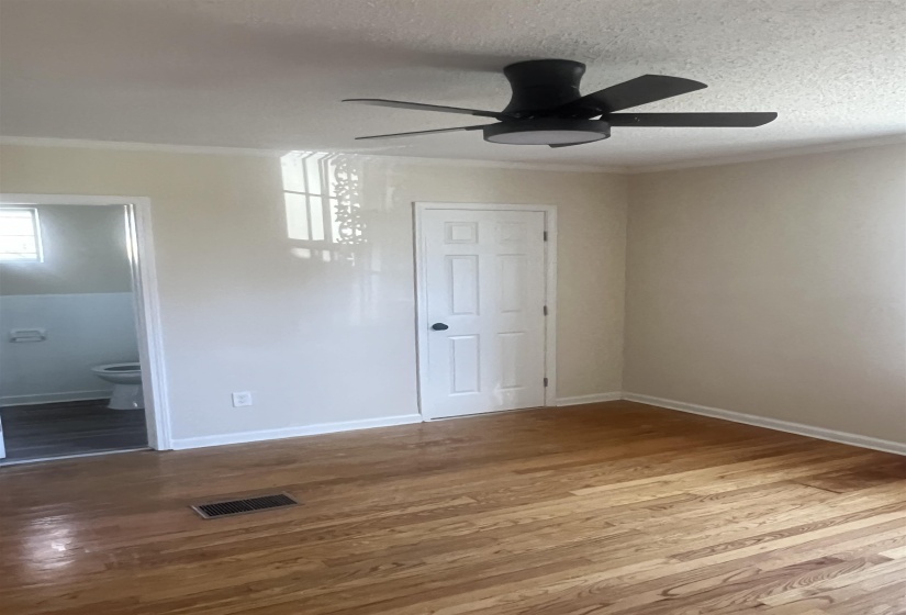 Unfurnished bedroom with ceiling fan, wood finished floors, ornamental molding, ensuite bathroom, and a textured ceiling