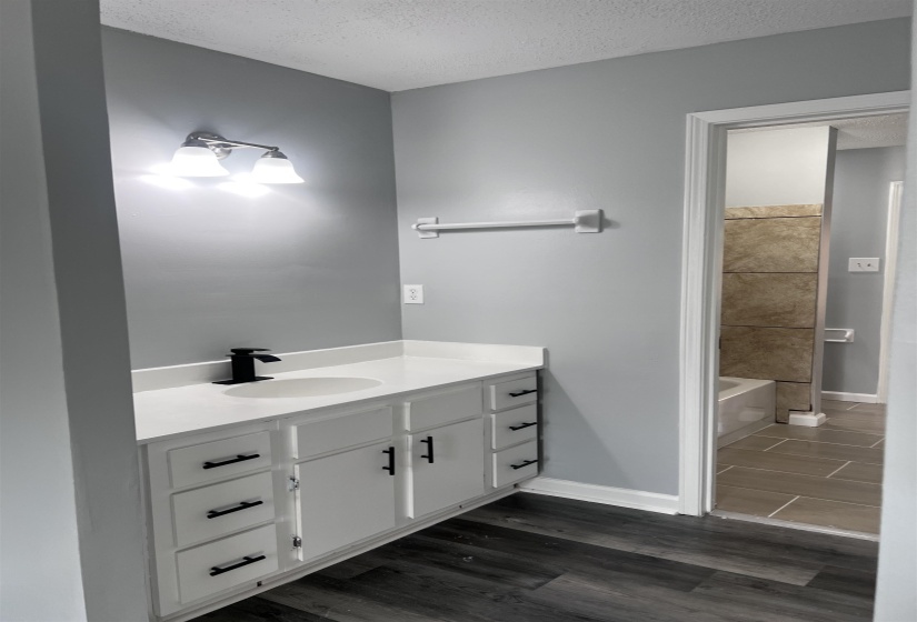 Bathroom featuring vanity, a textured ceiling, dark wood-style floors, and a tub