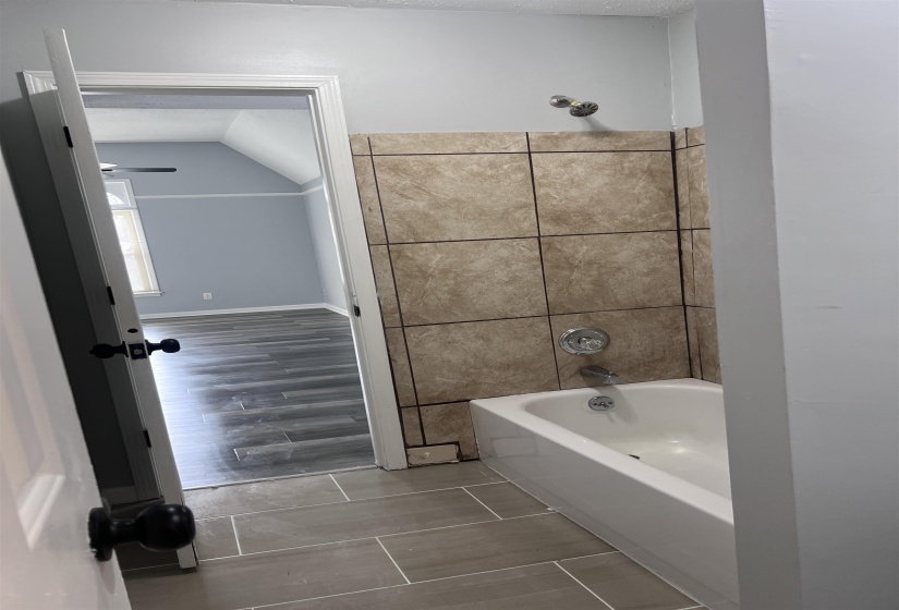 Bathroom with washtub / shower combination, vaulted ceiling, and wood finish floors