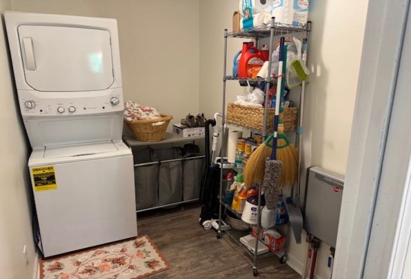 Washroom with stacked washer and clothes dryer, dark wood-style flooring, and heating unit