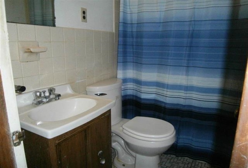 Bathroom featuring tile walls, toilet, vanity, and a shower with curtain