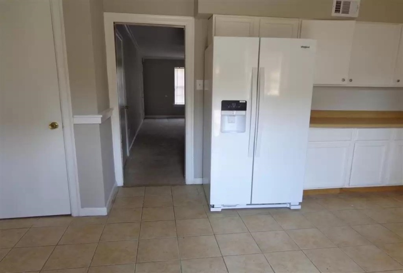 Kitchen with white refrigerator with ice dispenser, white cabinetry, light tile patterned floors, and baseboards