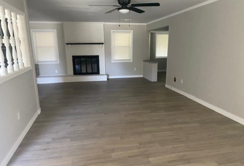Unfurnished living room with a ceiling fan, baseboards, crown molding, a fireplace, and wood finished floors