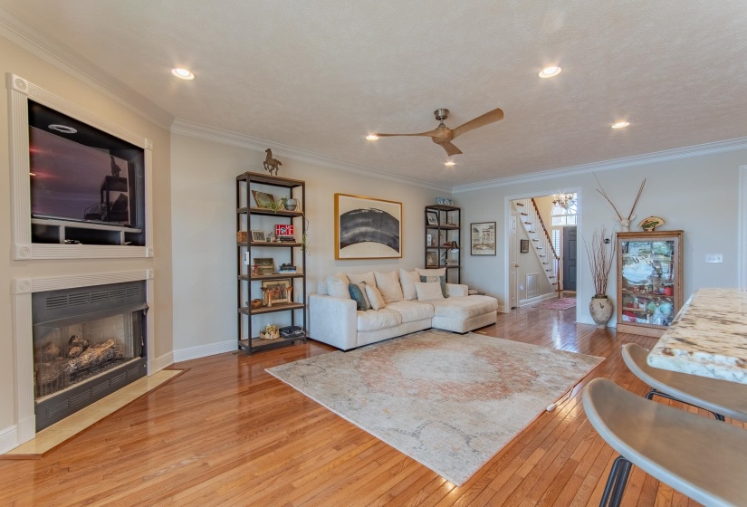 Living room featuring stairs, crown molding, a fireplace with flush hearth, and hardwood / wood-style flooring