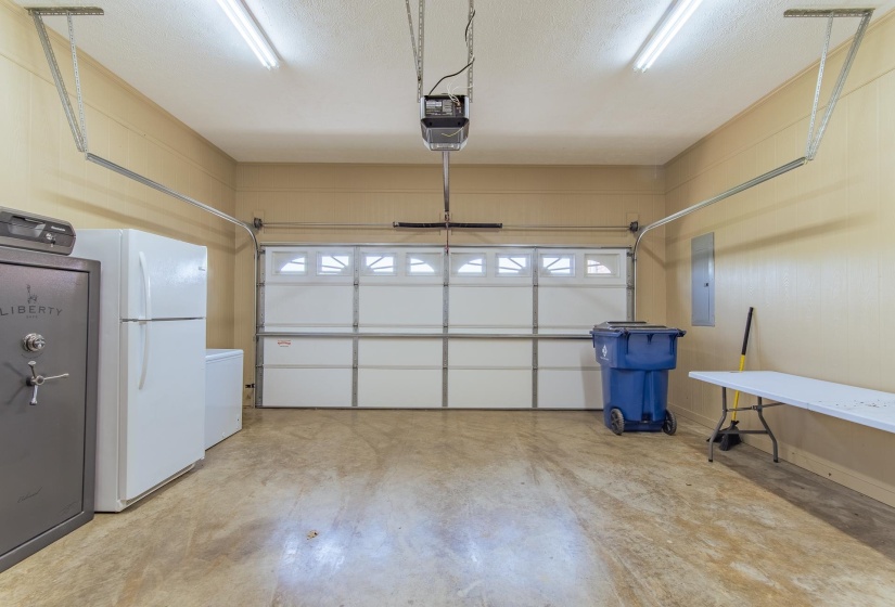Garage with a garage door opener, freestanding refrigerator, and electric panel