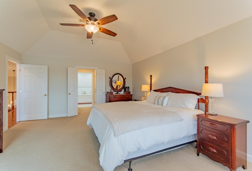 Bedroom with lofted ceiling, light carpet, baseboards, ceiling fan, and connected bathroom