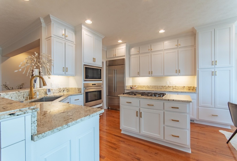 Kitchen featuring light stone countertops, white cabinetry, a sink, built in appliances, and light wood-style flooring