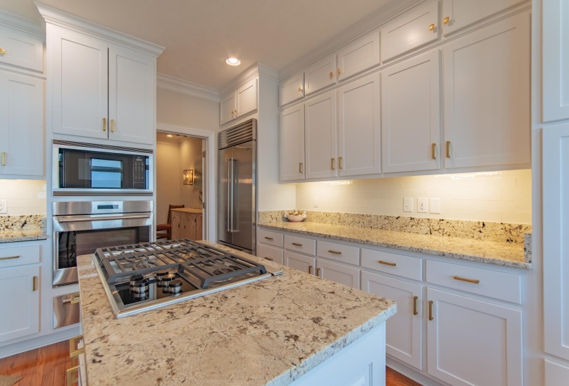 Kitchen featuring tasteful backsplash, light stone counters, built in appliances, recessed lighting, and white cabinetry
