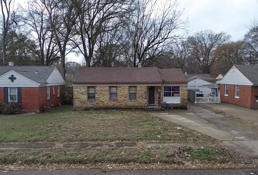 Ranch-style home with a front yard, brick siding, driveway, and view of scattered trees