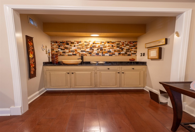 Indoor wet bar with dark wood finished floors, decorative backsplash, cream cabinets, and dark stone countertops