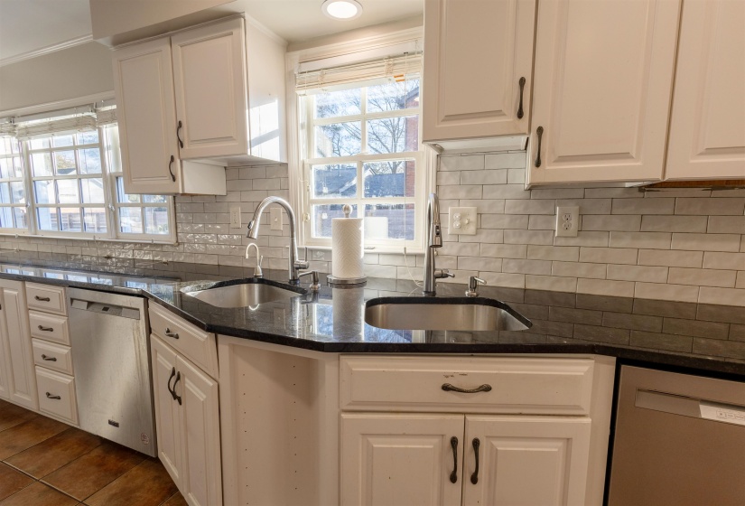 Kitchen with stainless steel dishwasher, white cabinets, and dark stone countertops