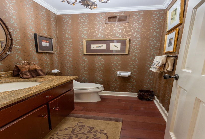 Bathroom with dark wood-type flooring, vanity, crown molding, and wallpapered walls
