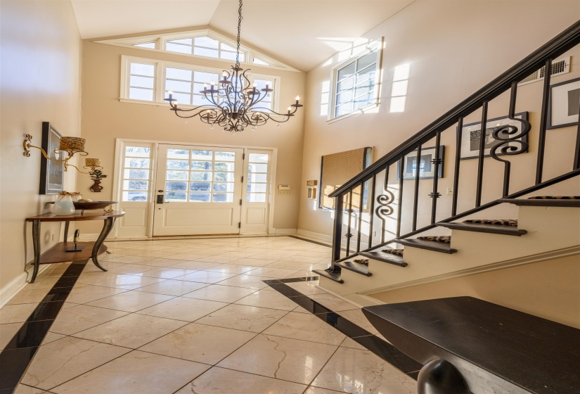 Entrance foyer with inlaid floor details, light marble finish flooring, a chandelier, stairs, and high vaulted ceiling