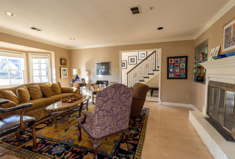 Living area featuring a fireplace, light wood finished floors, crown molding, stairs, and recessed lighting