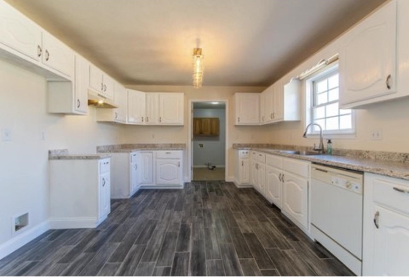 Kitchen with dishwasher, wood tiled floors, white cabinetry, light countertops, and under cabinet range hood
