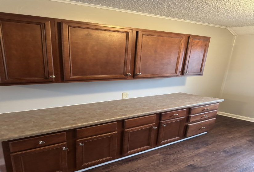 Kitchen with dark wood-type flooring, a textured ceiling, light countertops, and crown molding