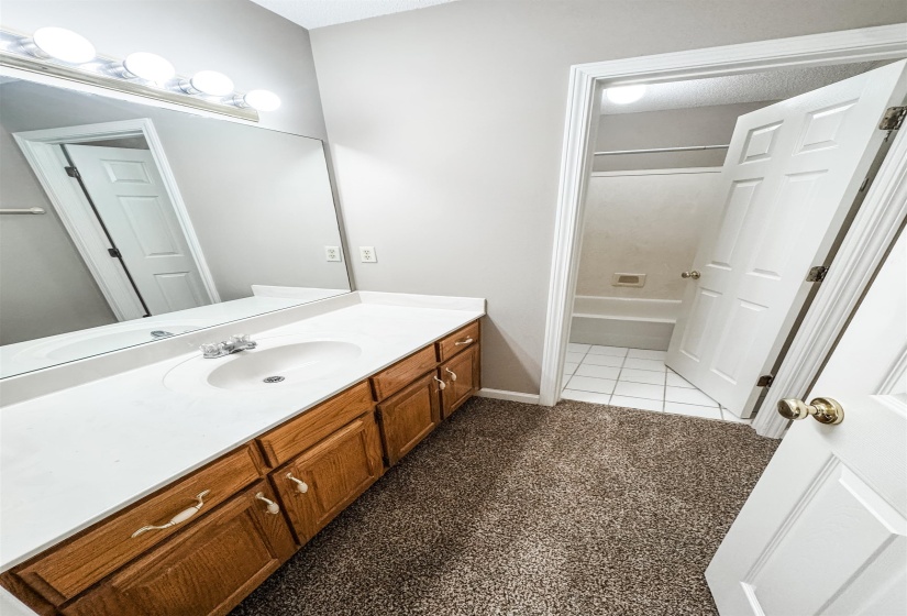 Full bath featuring vanity, light carpet, shower / tub combination, and light tile patterned flooring