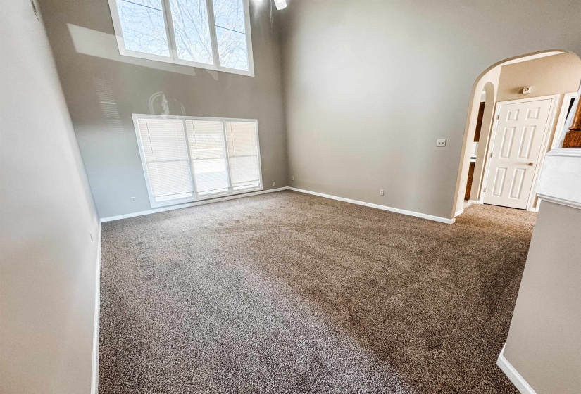 Carpeted spare room with arched walkways, a high ceiling, and healthy amount of natural light