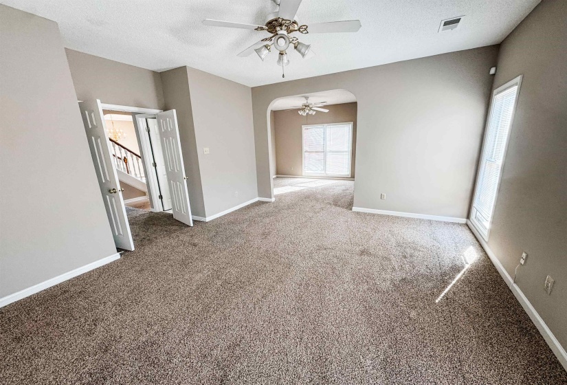 Carpeted empty room featuring a textured ceiling, arched walkways, a ceiling fan, and stairway