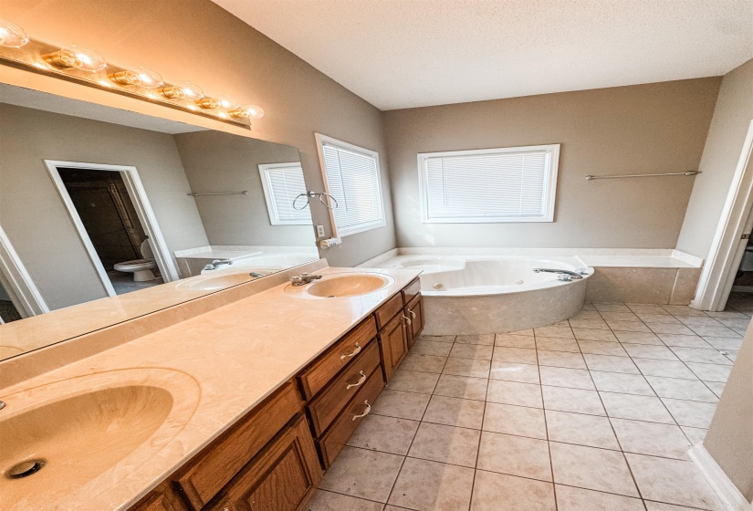 Full bath with double vanity, a garden tub, light tile patterned flooring, and a textured ceiling