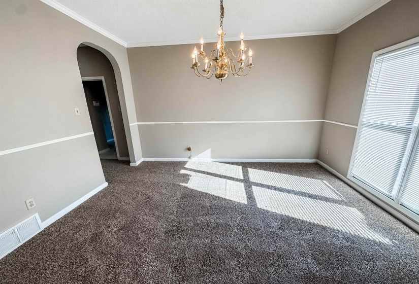 Empty room featuring arched walkways, dark colored carpet, ornamental molding, and a chandelier