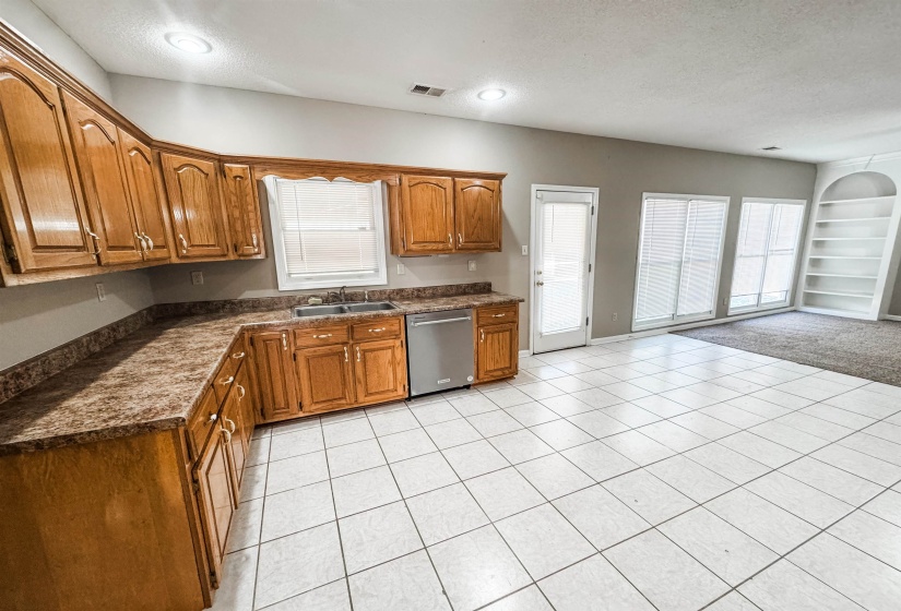 Kitchen with dark countertops, brown cabinets, dishwasher, a textured ceiling, and built in features