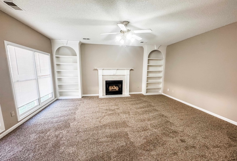 Unfurnished living room with built in shelves, a textured ceiling, a high end fireplace, carpet, and ceiling fan