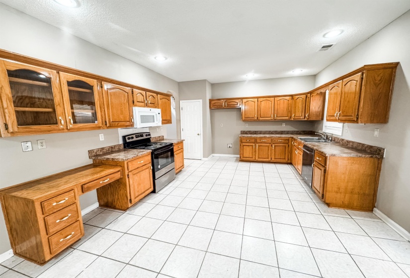 Kitchen featuring brown cabinets, stainless steel electric stove, dark countertops, white microwave, and recessed lighting