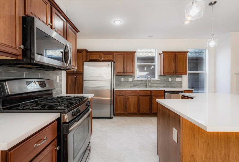 Kitchen with appliances with stainless steel finishes, brown cabinets, backsplash, pendant lighting, and recessed lighting