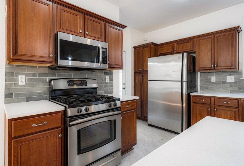 Kitchen with stainless steel appliances, backsplash, brown cabinets, and light stone counters